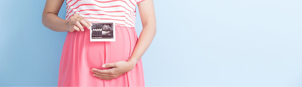 Pregnant woman holding sonogram photo in front of belly